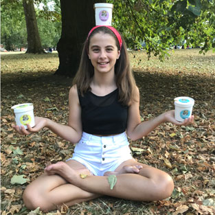 Girl in sitting yoga pose holding an Angels & Cookies cookie dough tub in each hand and balancing another on her head